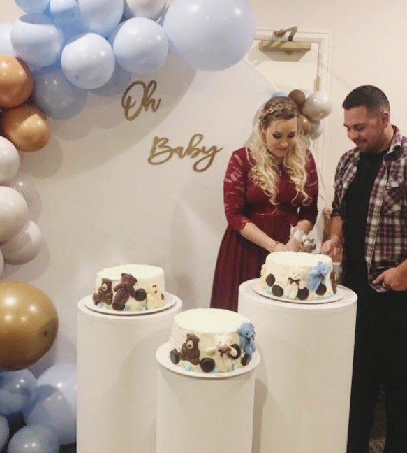 Expectant mother and father cutting a cake at a baby shower with balloons.