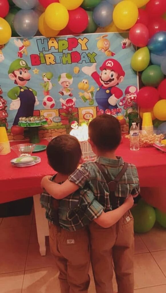 Two excited boys looking at a fun happy birthday sign featuring Mario Brothers with balloons and a cake