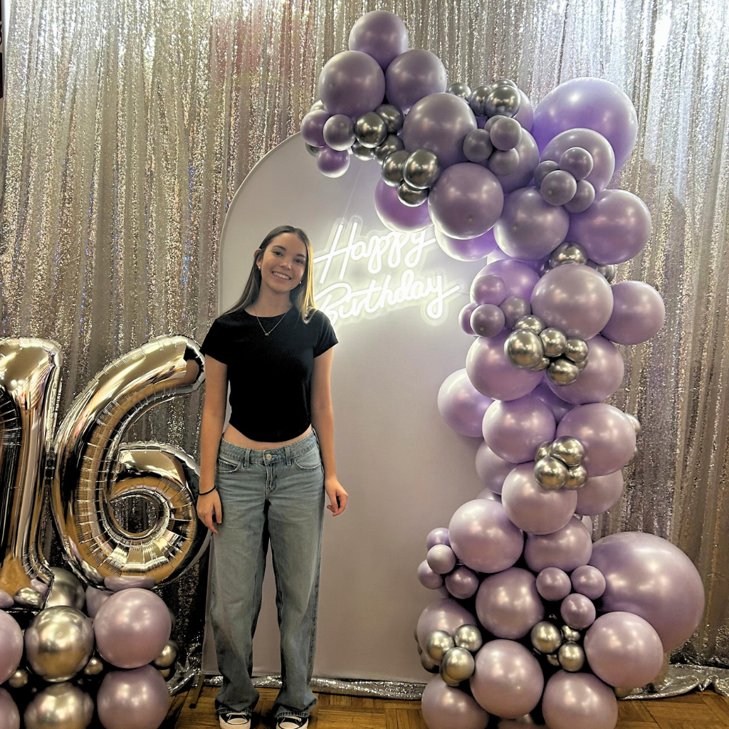 Young girl standing under a balloon arch at her Sweet 16 birthday party